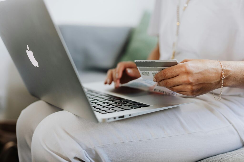 A person is seated with a silver laptop on their lap, entering payment details from a credit card into a premium ecommerce website, indicating an enhanced online shopping experience