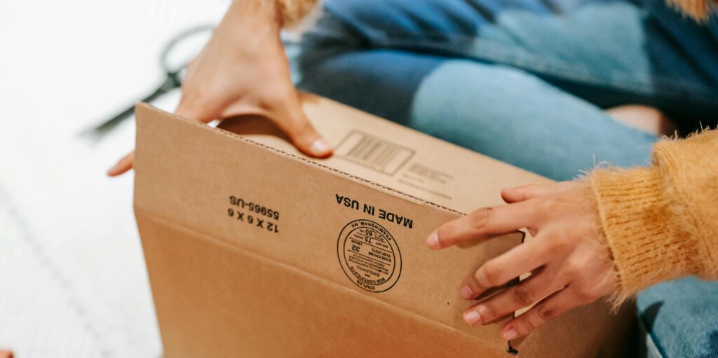 Close-up of a woman's hands securely sealing a cardboard shipping box, symbolizing the attention to detail needed in packing to meet customer shipping expectations.